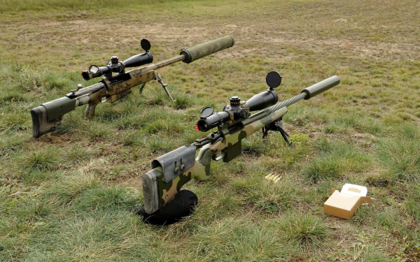 A high-definition desktop wallpaper featuring two sniper rifles on grassy terrain, showcasing detailed man-made design elements.