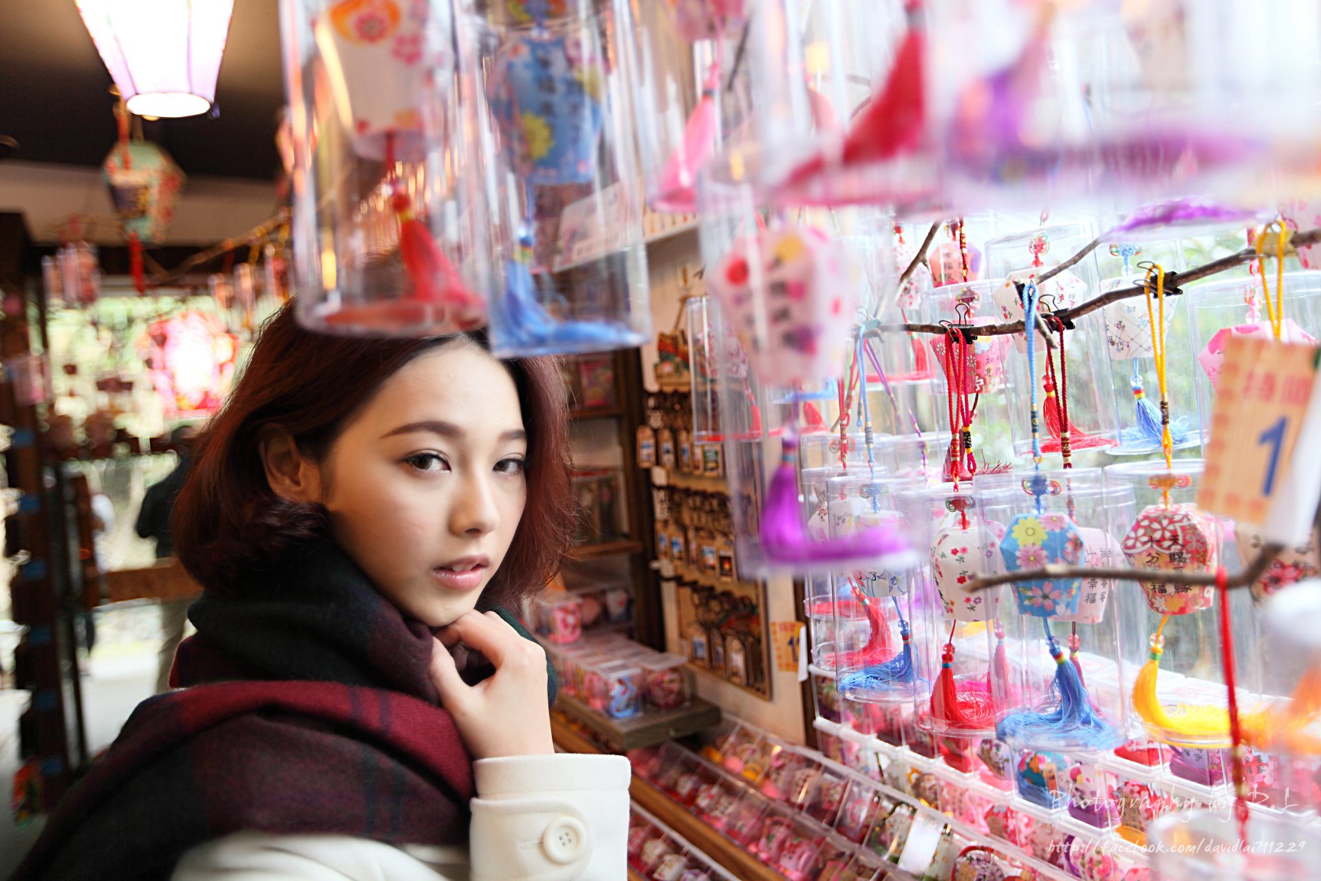 Taiwanese Asian model Lín Yǔ stands inside a vibrant shop filled with colorful hanging decorations and trinkets, captured in vivid 4K Ultra HD detail.