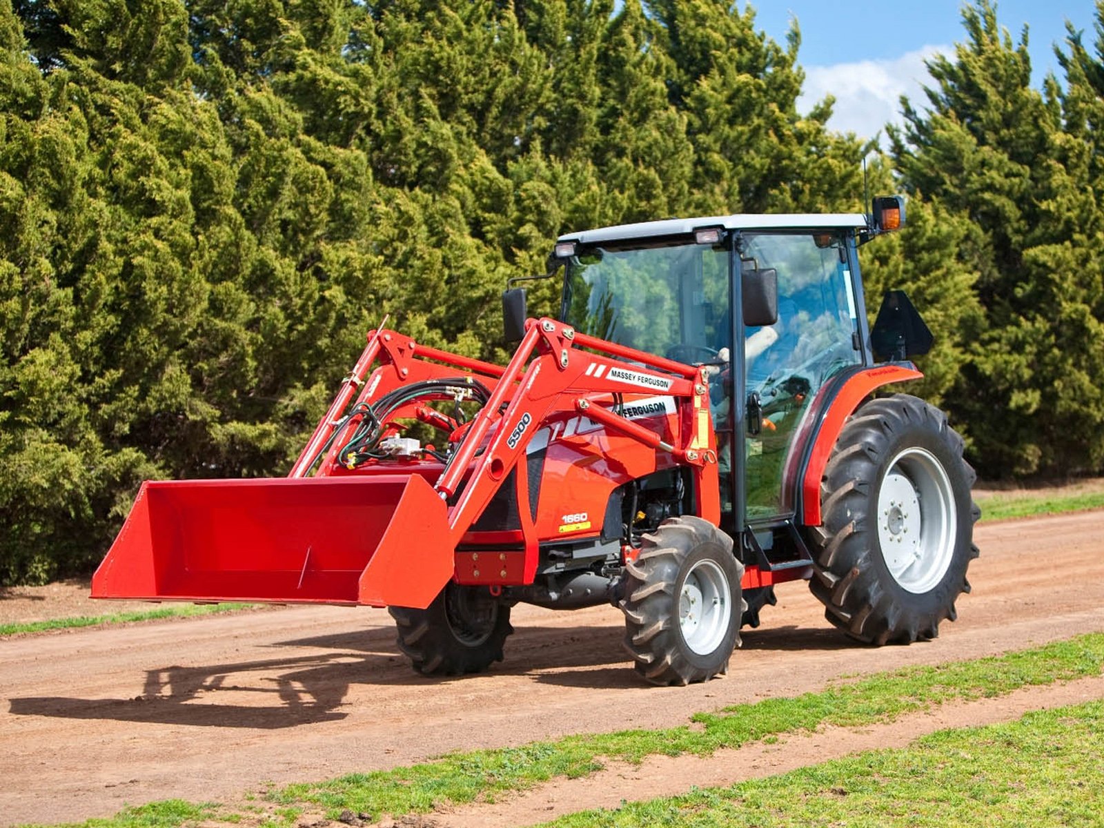 A vibrant Massey Ferguson tractor driving on a dirt road, surrounded by lush green trees, showcased as a high-definition desktop wallpaper and background.