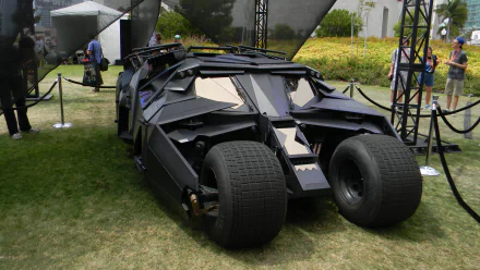 A striking image of the Batmobile on display, showcasing its sleek, futuristic design. This 4K Ultra HD wallpaper captures the vehicle in an outdoor setting, surrounded by greenery.