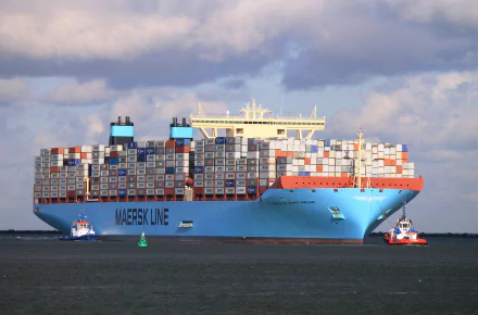 A large container ship, adorned with colorful cargo containers, is being assisted by tugboats against a backdrop of blue skies, creating a striking HD desktop wallpaper and background.