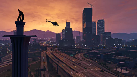 A stunning HD wallpaper from Grand Theft Auto V featuring a helicopter flying over a vibrant city skyline at sunset, with illuminated buildings and a winding highway below.