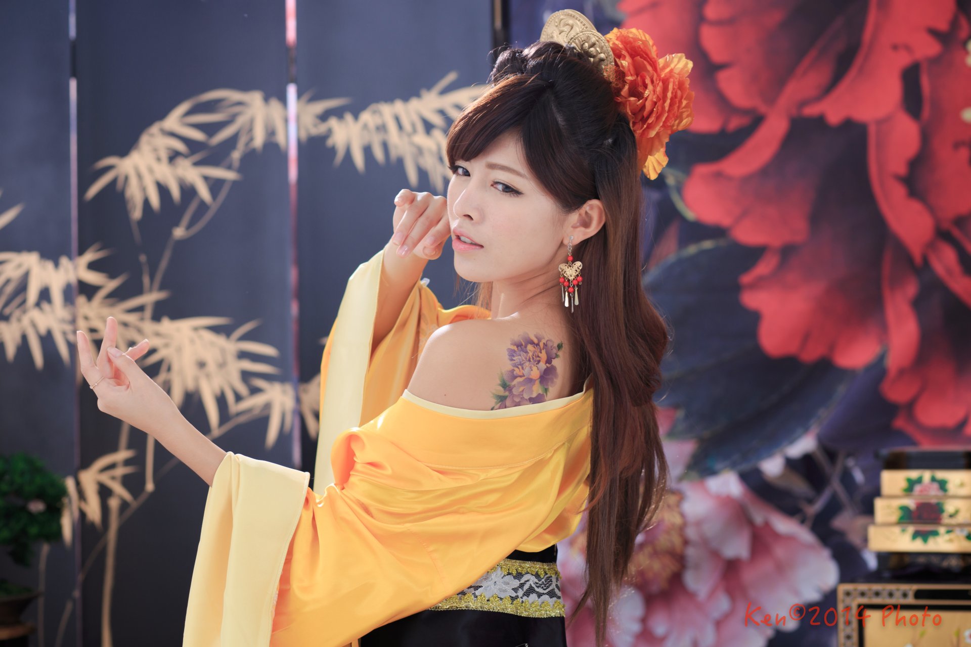 Woman in yellow traditional costume with ornate hair-dress, dangling earrings and a floral shoulder tattoo, captured in vibrant 5K Ultra HD desktop wallpaper.