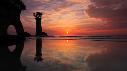 A serene beach at dusk, featuring a vibrant sunset reflected in calm waters, with silhouettes of rocky formations against a colorful twilight sky.