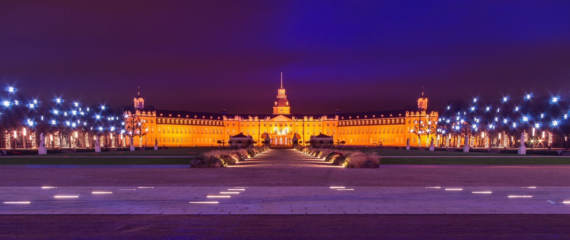 Man-made Karlsruhe Palace illuminated at night, captured as a wide 2K Quad HD PC desktop wallpaper/background showing the central facade and lit promenade.