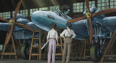 HD wallpaper of two characters from The Wind Rises standing in front of a vintage airplane inside a hangar.