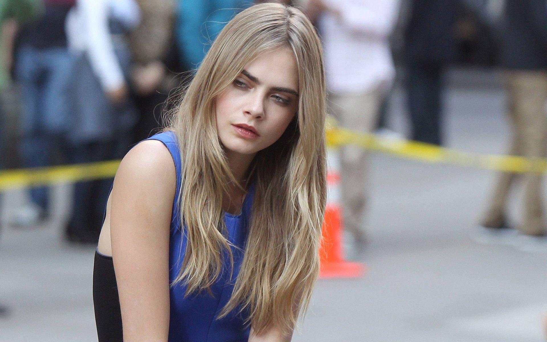 A striking HD desktop wallpaper featuring model and celebrity Cara Delevingne, captured in a candid moment with a blurred urban backdrop.