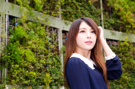 4K Ultra HD desktop wallpaper of a Taiwanese Asian model: a woman in a navy dress with a white collar posing by a leafy green fence, gazing softly toward the light.