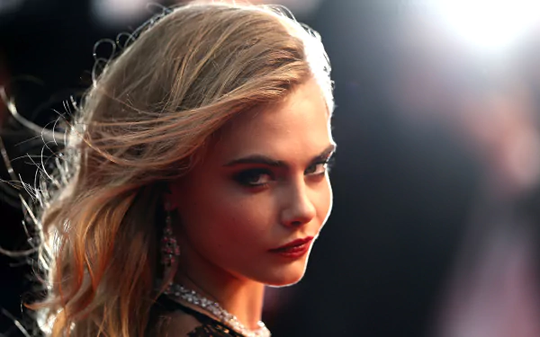 A captivating HD wallpaper featuring Cara Delevingne, showcasing her striking profile and glamorous style against a blurred, vibrant background.