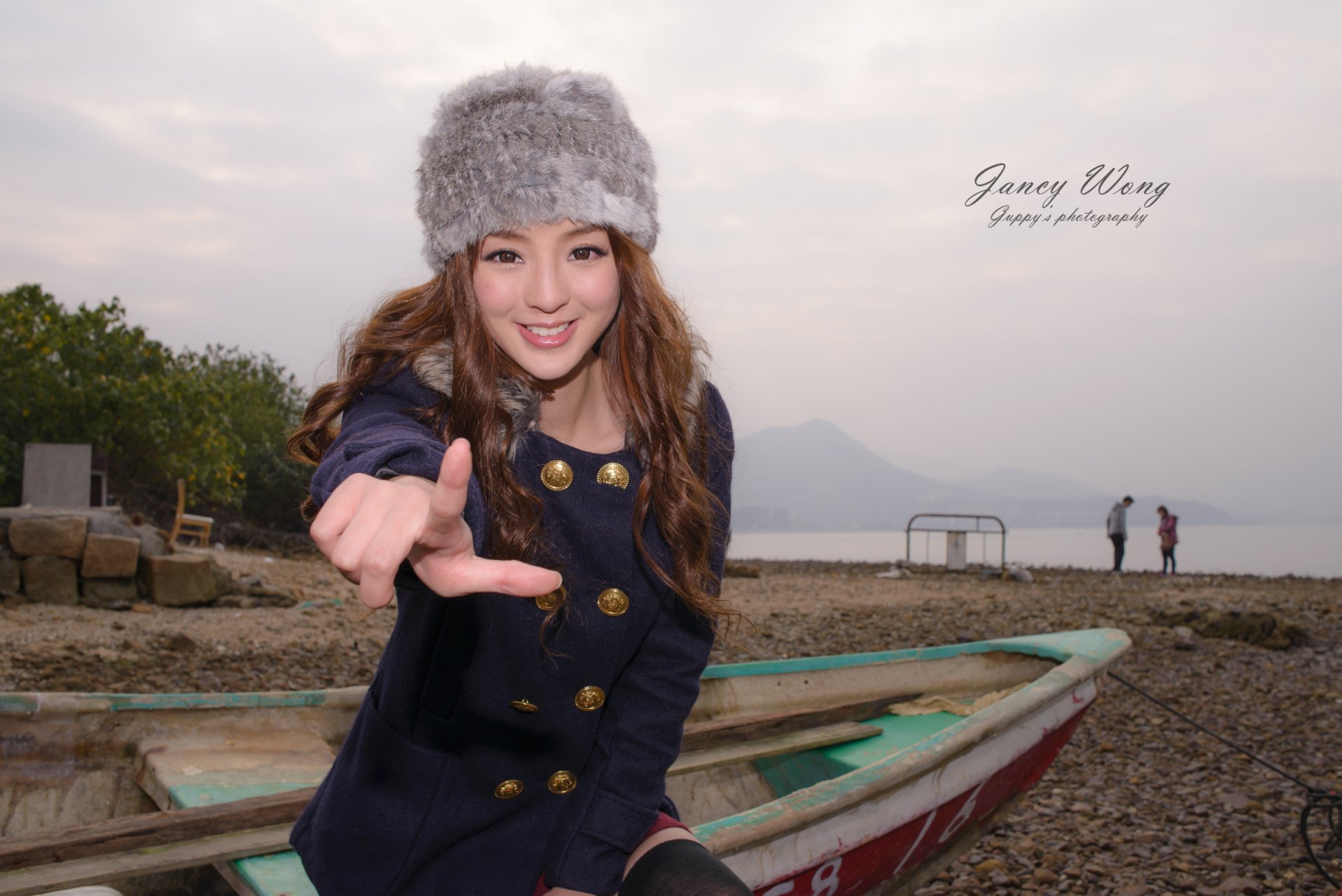 A smiling Asian woman wears a stylish cap while posing by a boat in Hong Kong. Captured by Jancy Wong, this HD image showcases a serene coastal vibe.