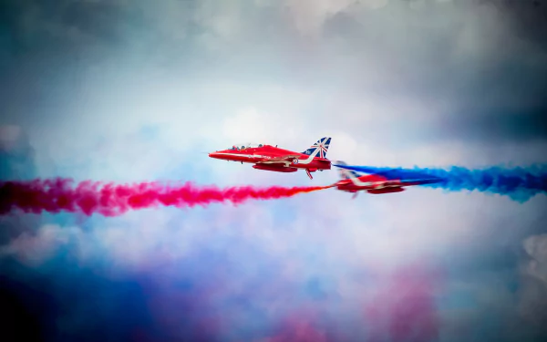 Two military aircraft perform in an air show, releasing vibrant red and blue smoke against a cloudy sky. This stunning image serves as a vibrant 4K Ultra HD desktop wallpaper.