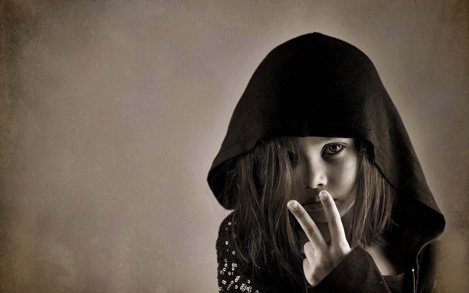HD desktop wallpaper features a cute child in a dark hooded garment, captured in expressive photography with a neutral background.