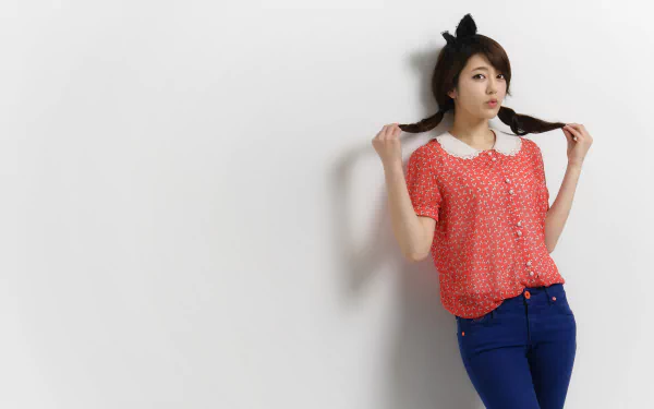 HD desktop wallpaper featuring an Asian woman with plaited hair and cat ears, wearing a red shirt with white polka dots and blue pants, posing against a plain white background.