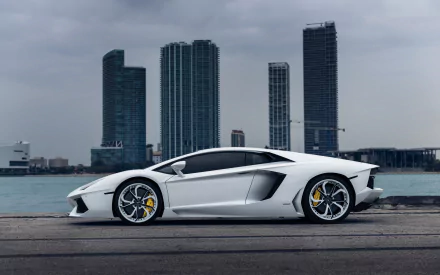 White Lamborghini Aventador sports car parked by the waterfront with city skyscrapers in the background, captured in a high-definition desktop wallpaper style.