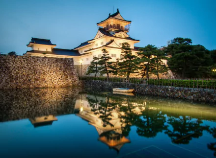Twilight view of Toyama Castle in Japan reflected in a calm pond, with a small boat floating nearby, captured in stunning 4K Ultra HD quality.