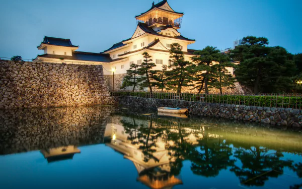 Twilight view of Toyama Castle in Japan reflected in a calm pond, with a small boat floating nearby, captured in stunning 4K Ultra HD quality.