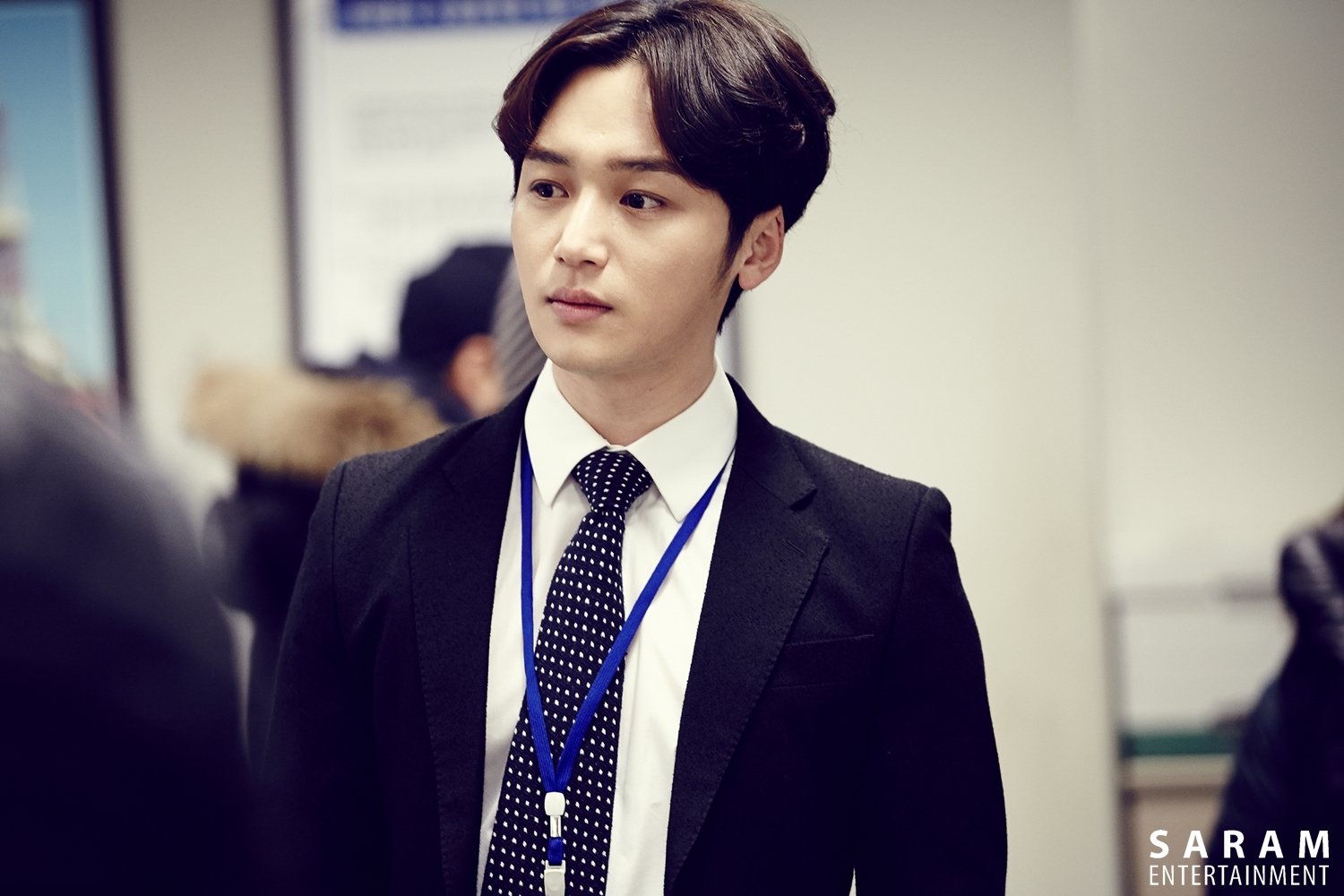 A man in a formal suit with a tie and ID badge, looking serious in a candid moment, serves as an engaging HD desktop wallpaper for fans of actors.
