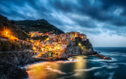 Nighttime time-lapse view of Manarola in Cinque Terre, Liguria, Italy, showcasing coastal cliffs, illuminated buildings, and dramatic clouds over the sea in 4K Ultra HD.
