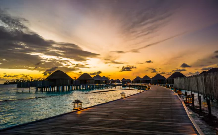 A serene dawn at Constance Halaveli Resort in the Maldives, showcasing a tropical pier with lanterns against a stunning sky, capturing the beauty of sunrise in this tranquil setting.