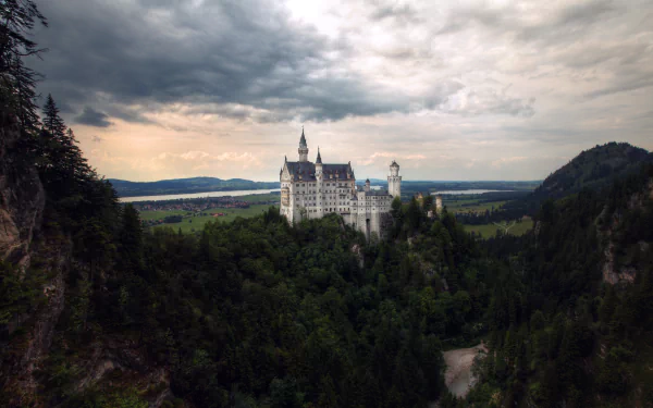 Neuschwanstein Castle perched above a Bavarian forest under dramatic clouds, panoramic landscape view — 5K Ultra HD PC desktop wallpaper.