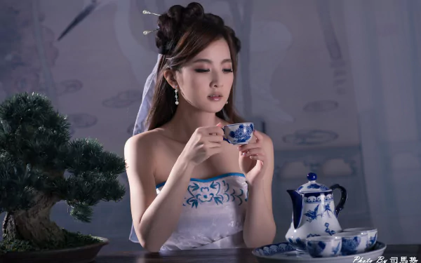 A serene Asian woman in traditional attire enjoys tea from a delicate cup, surrounded by a bonsai and a beautiful tea set, set in an elegant atmosphere.
