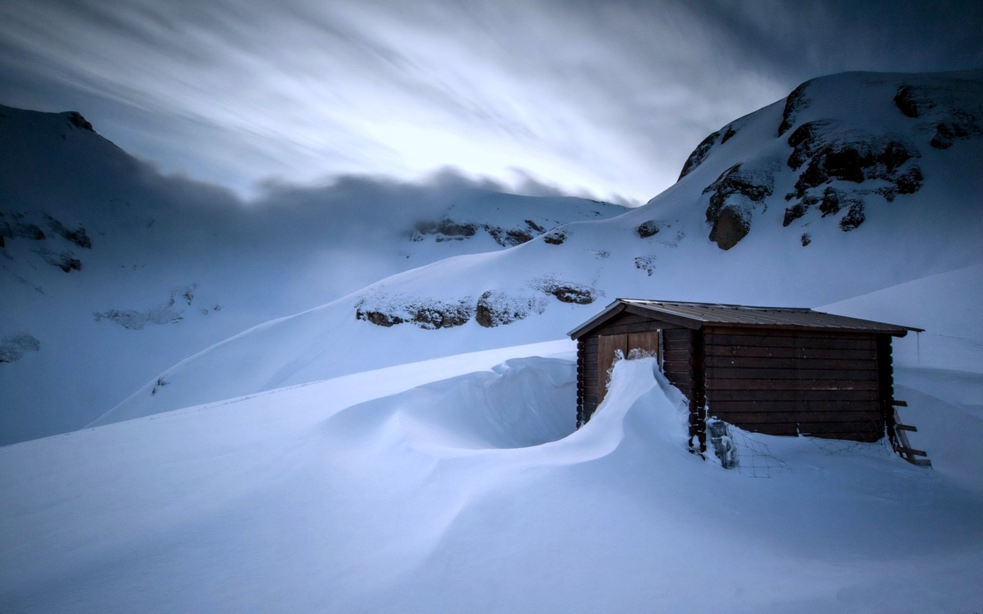 Snow-covered wooden hut nestled in a cold, mountainous landscape under a cloudy sky, captured in stunning 4K Ultra HD winter nature photography.