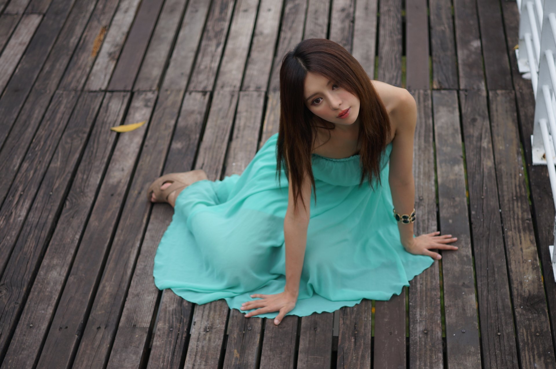 Taiwanese model Julie Chang in a flowing turquoise dress and bracelet, seated on weathered wooden planks, captured in a 4K Ultra HD desktop wallpaper.