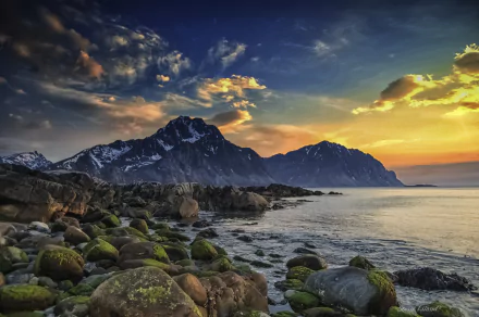 A stunning view of the Lofoten Islands in Norway, featuring dramatic mountains, a rocky seashore with moss-covered boulders, and a vibrant sky at sunset, capturing the essence of Arctic spring.