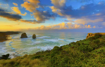 Dawn breaks over the Twelve Apostles limestone stacks along the Victoria coastline in Australia, with vibrant clouds and the sea creating a stunning natural landscape.