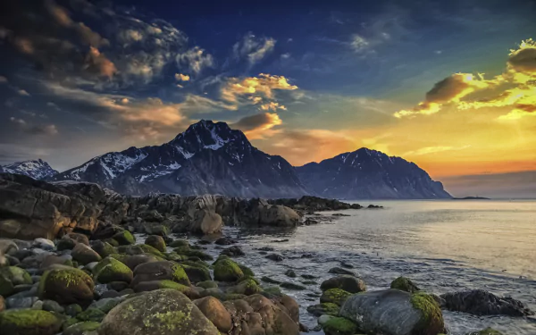 A stunning view of the Lofoten Islands in Norway, featuring dramatic mountains, a rocky seashore with moss-covered boulders, and a vibrant sky at sunset, capturing the essence of Arctic spring.
