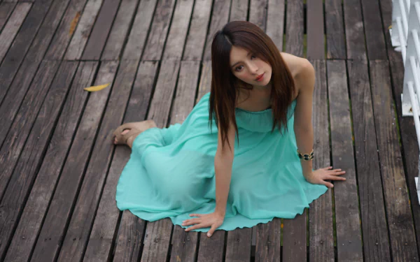 Taiwanese model Julie Chang in a flowing turquoise dress and bracelet, seated on weathered wooden planks, captured in a 4K Ultra HD desktop wallpaper.
