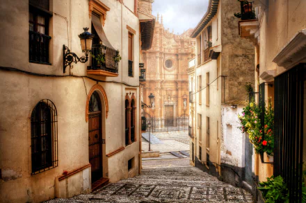 Narrow cobblestone street in Guadix, Andalusia, Spain, lined with houses and lanterns, leading to the historic Guadix Cathedral in the province of Granada.