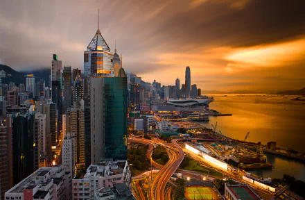 A stunning sunset over Victoria Harbour, showcasing the vibrant architecture and skyline of Hong Kong's megapolis, with warm light reflecting on the water and city.