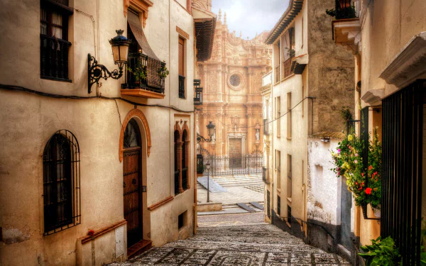 Narrow cobblestone street in Guadix, Andalusia, Spain, lined with houses and lanterns, leading to the historic Guadix Cathedral in the province of Granada.