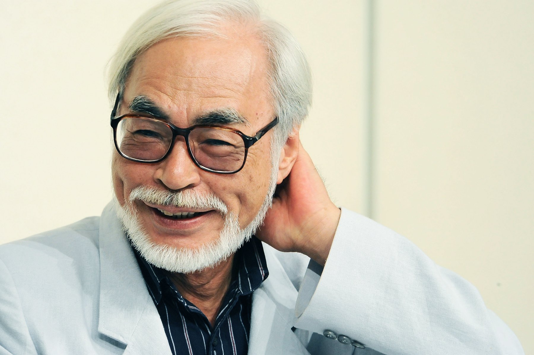 HD desktop wallpaper featuring a smiling, bespectacled person related to Hayao Miyazaki.