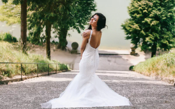A brunette bride models an elegant wedding dress, posing gracefully on a stone pathway surrounded by greenery. This HD image captures a beautiful, serene moment in nature.