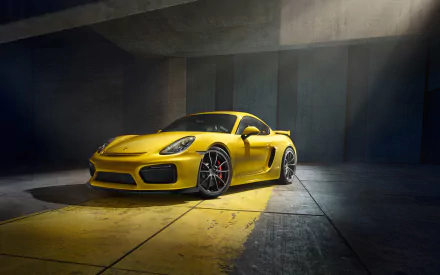 A vibrant yellow Porsche Cayman GT4 sports car illuminated in a dimly lit, industrial setting, captured in high definition for a desktop wallpaper background.