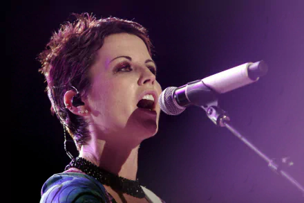 HD PC desktop wallpaper of a female singer mid-performance, close-up at a microphone under purple stage lighting, an expressive, intense musical portrait.