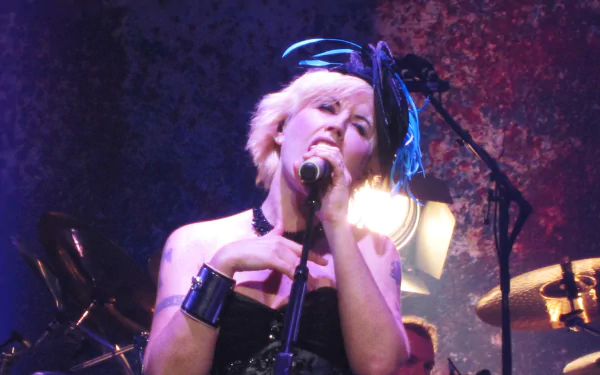 Female singer performing onstage, gripping a microphone with drums behind, vivid colored lighting and textured backdrop — 4K Ultra HD PC desktop music wallpaper.