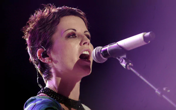 HD PC desktop wallpaper of a female singer mid-performance, close-up at a microphone under purple stage lighting, an expressive, intense musical portrait.