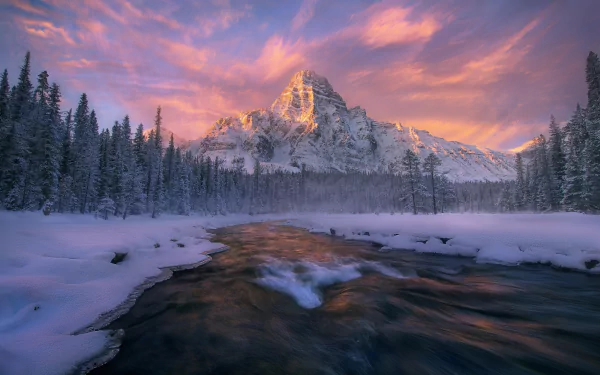 A stunning winter scene in Banff National Park, Canada, featuring a serene river surrounded by snow-covered forests and majestic mountains under a colorful sky.
