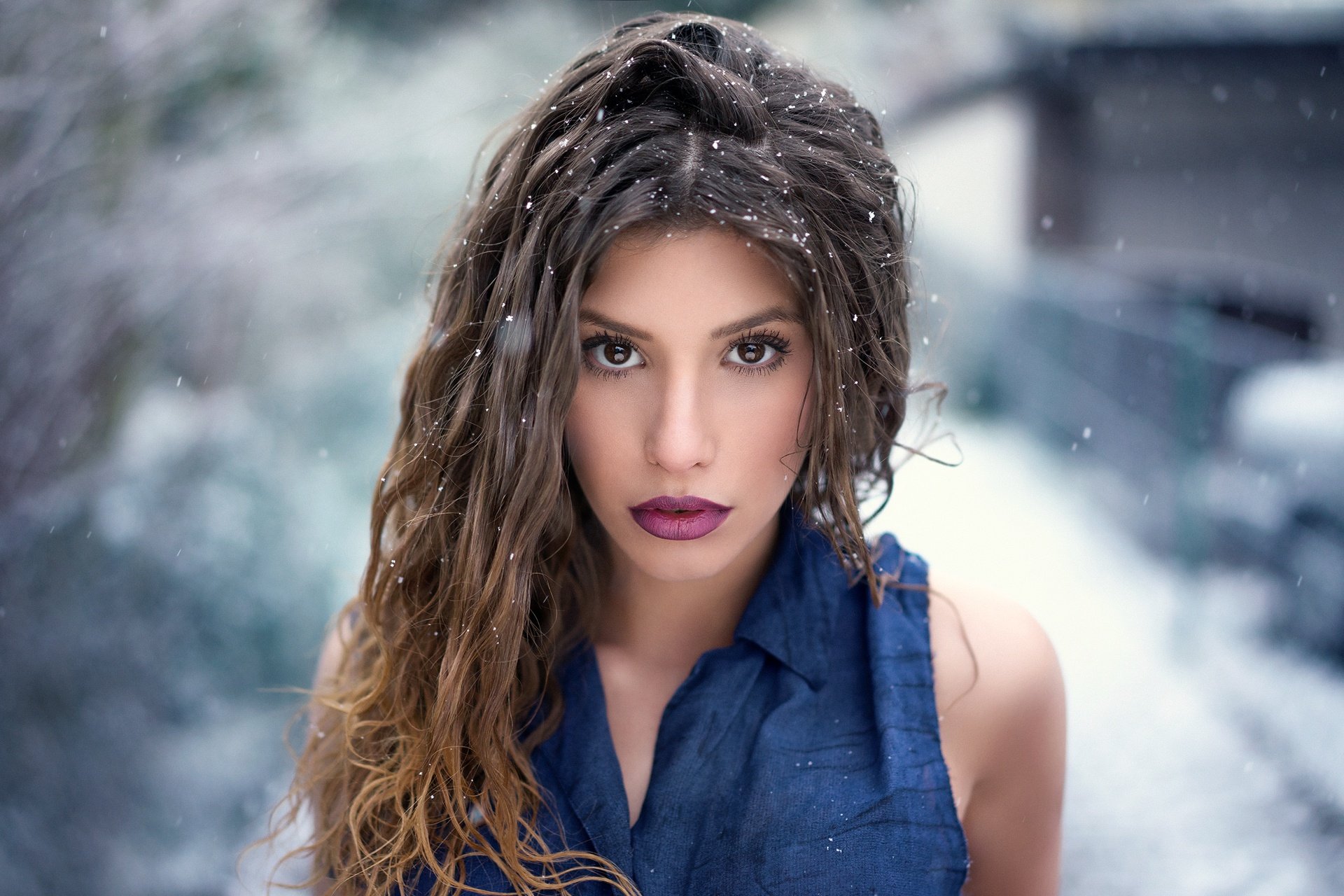 A brunette woman with brown eyes and bold lipstick stands confidently in the snow, captured in a striking HD desktop wallpaper.