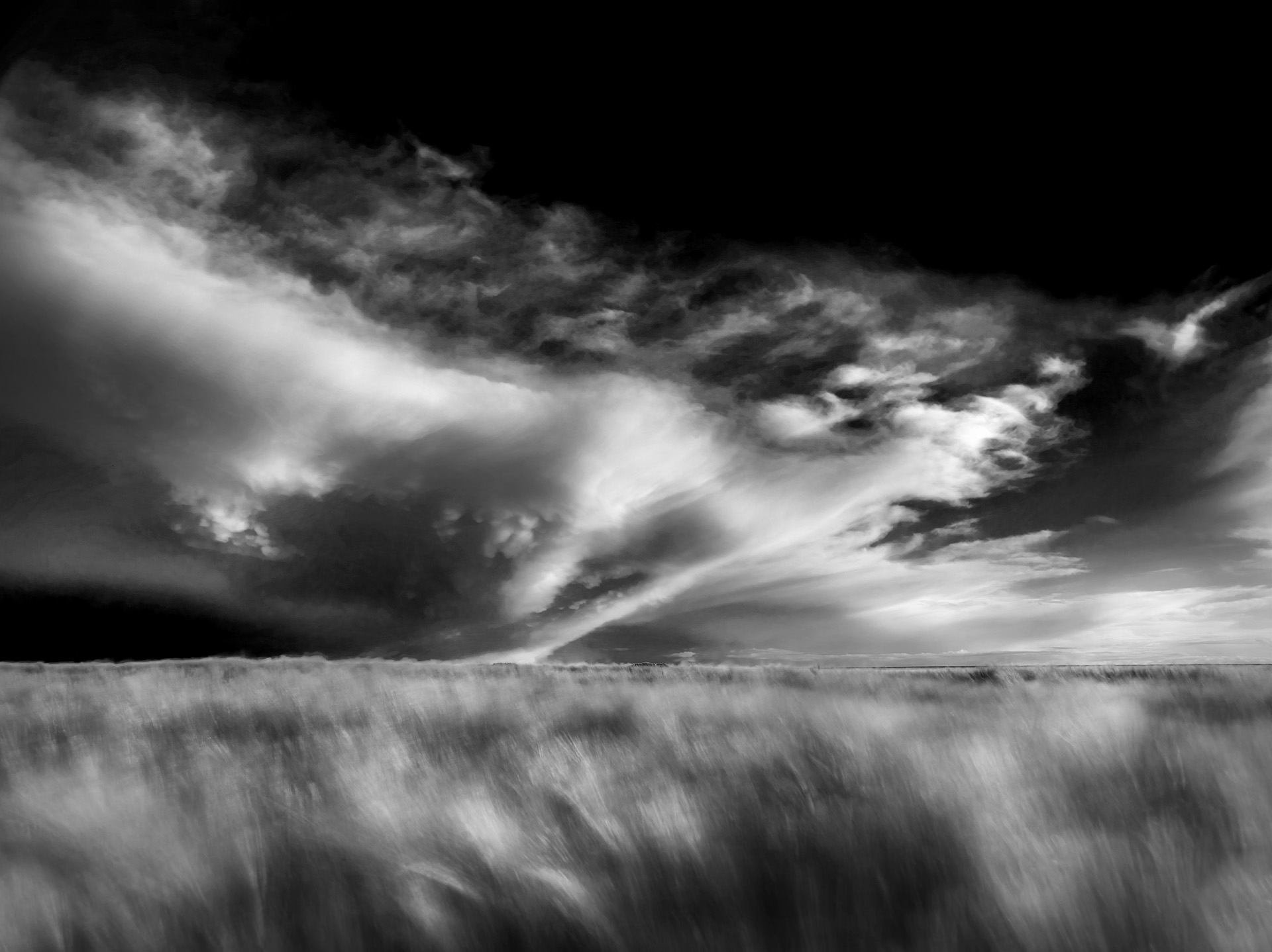 Black and white HD desktop wallpaper featuring a dramatic cloudscape over a vast field, capturing the raw beauty of nature in a striking landscape.