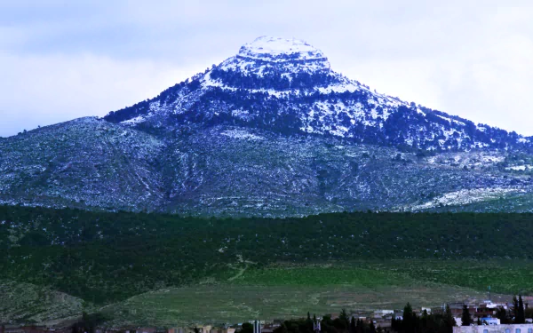 Snow-capped Tebessa Mountains rise above dense forests in Algeria's Amazigh Mountain range, captured in this HD landscape photography.