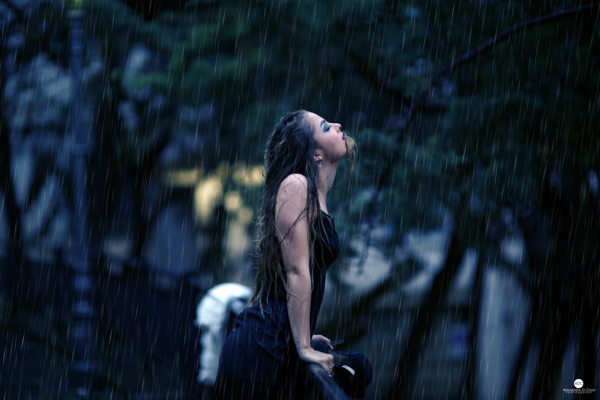 A woman stands in the rain, head tilted upward with a melancholic expression. The dark, rainy background enhances the moodiness. HD desktop wallpaper and background.