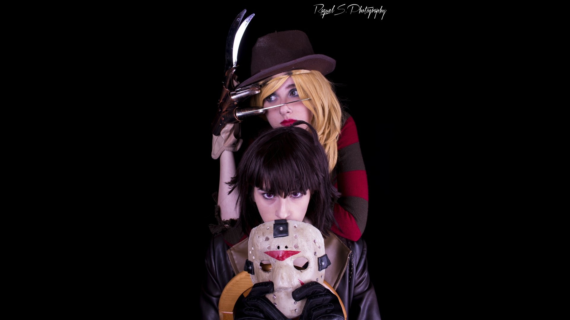 8K Ultra HD PC desktop wallpaper of two women in cosplay: one in a fedora with a bladed glove behind another holding a cracked hockey mask, set against a deep black background.