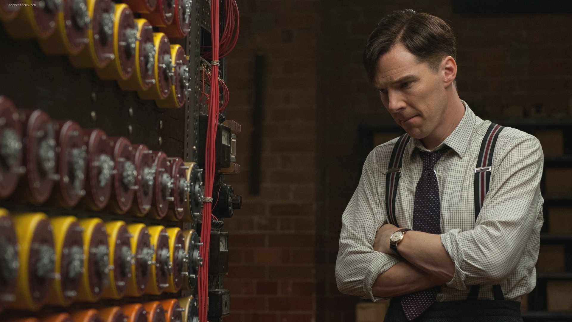 HD desktop wallpaper: brooding man in 1940s shirt and suspenders beside rows of code wheels, scene from the movie The Imitation Game.