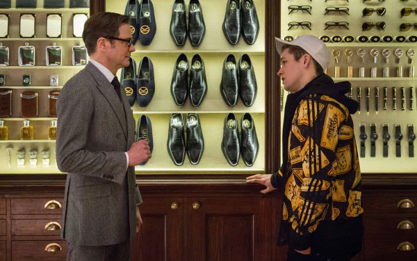 Taron Egerton and Colin Firth converse in a stylish setting filled with shoes and gadgets, capturing a moment from the movie Kingsman: The Secret Service. 4K Ultra HD wallpaper.