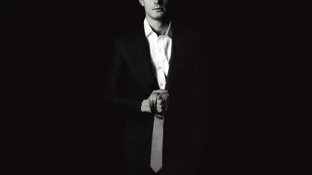 HD desktop wallpaper and background featuring Jamie Dornan from the movie Fifty Shades of Grey, wearing a suit and holding a necktie against a dark background.