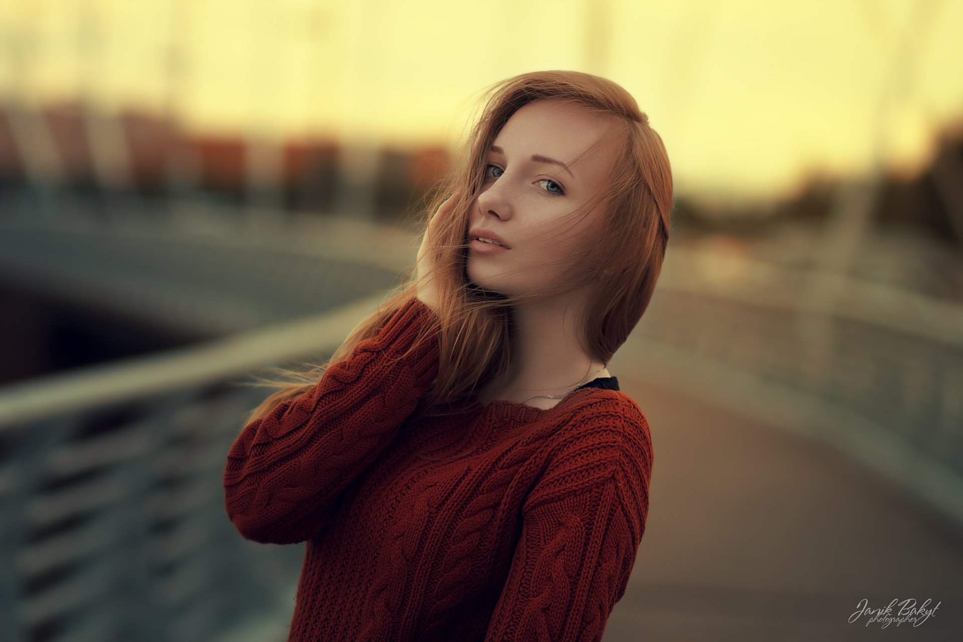 HD PC wallpaper featuring a blonde blue-eyed woman model with a red sweater, posed against a softly blurred bokeh background.